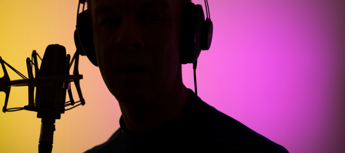 Silhouette of a man learning how to be a voice actor in 2024, over a yellow and purple background. 